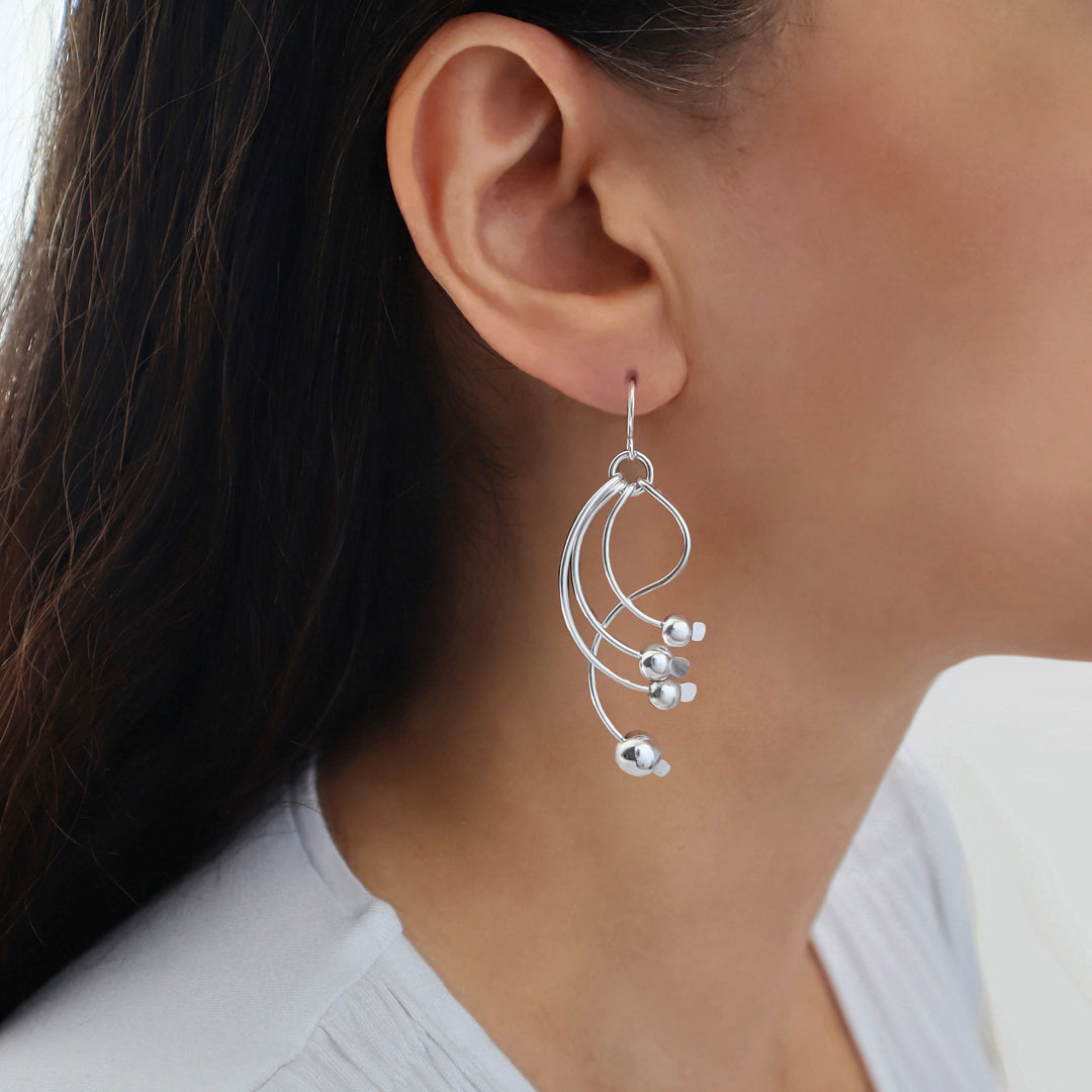 A close-up of a woman's ear wearing a 925 silver dangle earring with abstract curved loops and small ball bead accents.
