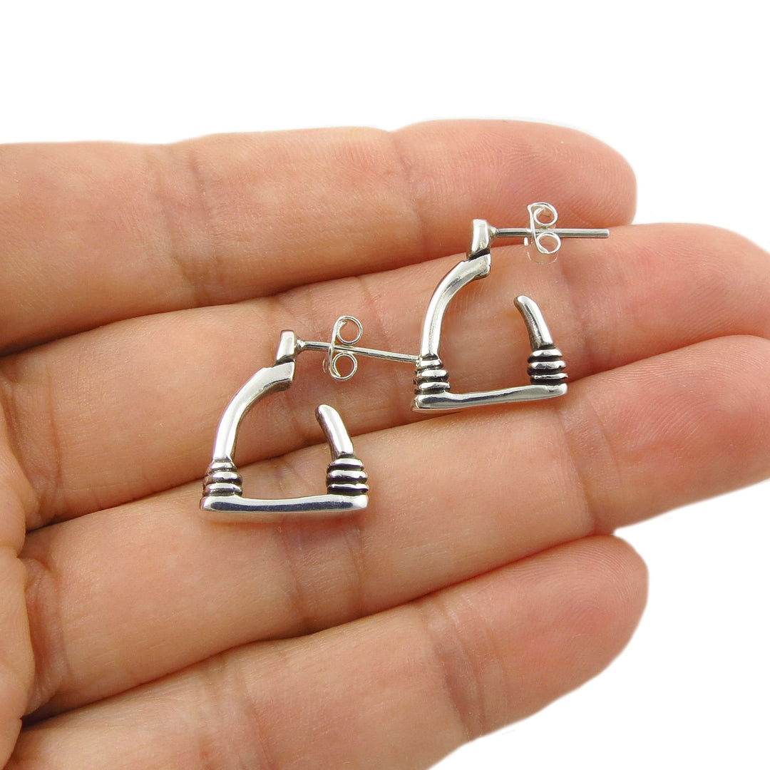 A pair of silver hoop earrings designed like textured equestrian horse stirrups, shown resting on an open hand against a white background.