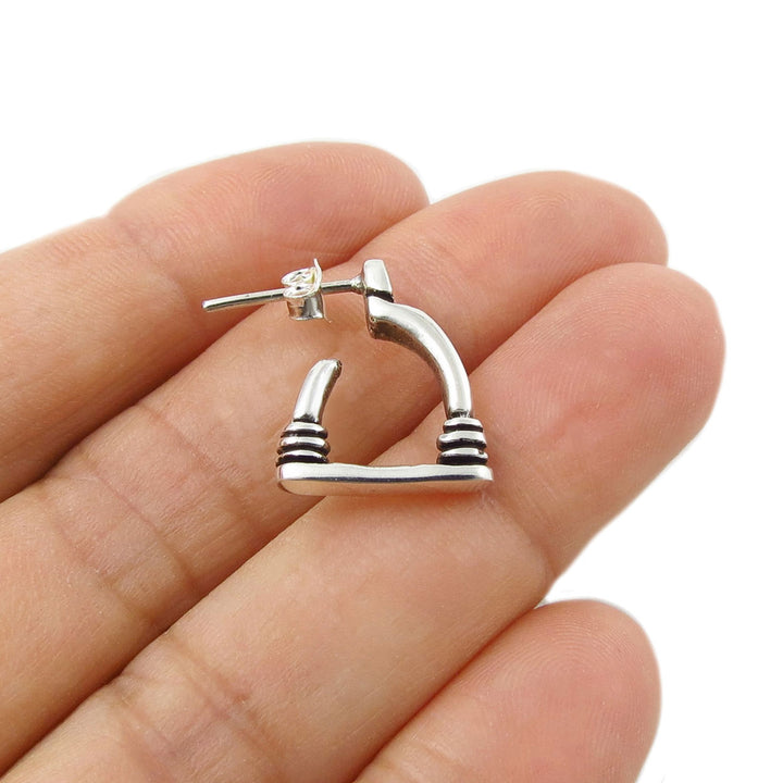 A small single 925 sterling silver horse stirrup design earring with horizontal striped details on the ends, shown resting on a person's fingers against a white background.