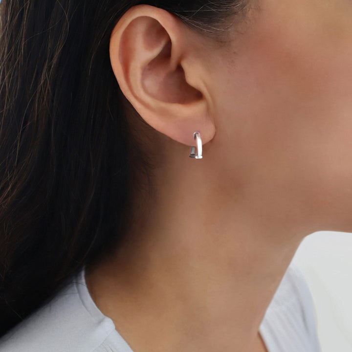 A close-up of a woman's ear wearing a small 925 sterling silver horse stirrup riding tack earring.