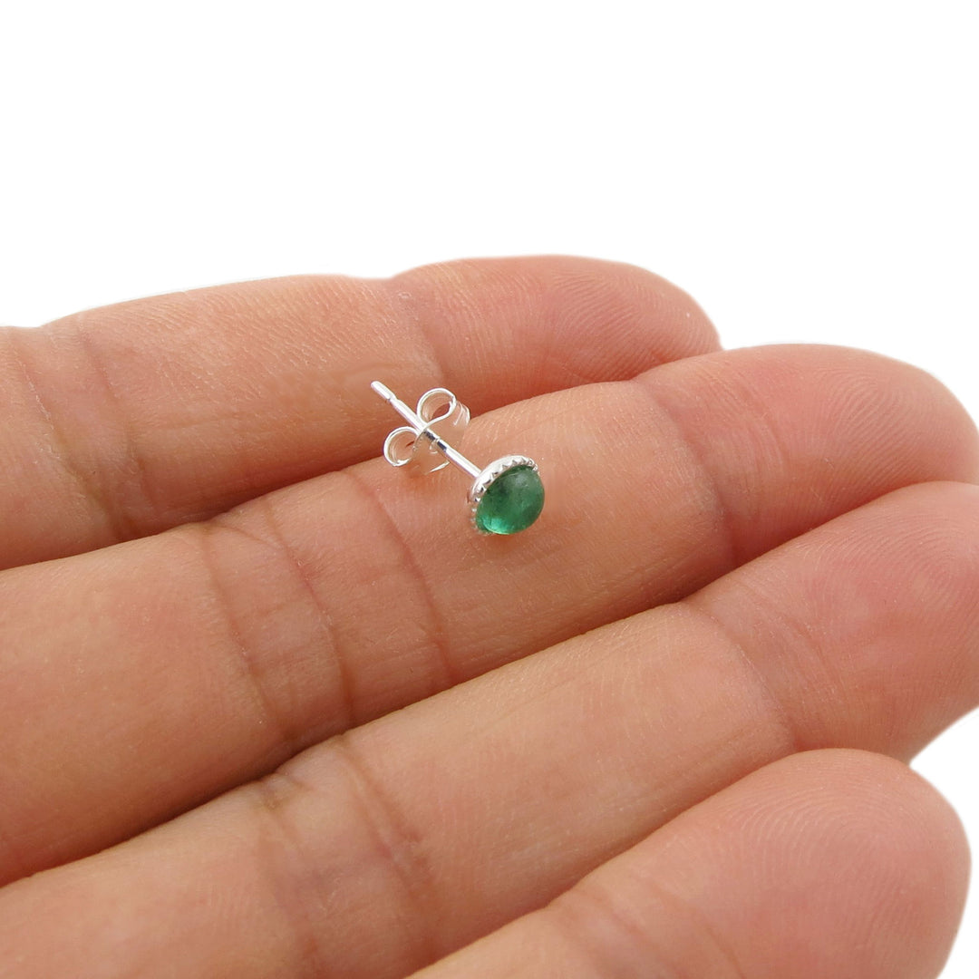 A single round-cut green natural emerald gemstone stud earring in a silver setting, shown resting on a person's palm for scale against a white background.