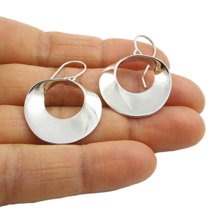 Solid 925 silver mobius strip hoop earrings held in a hand against a white background