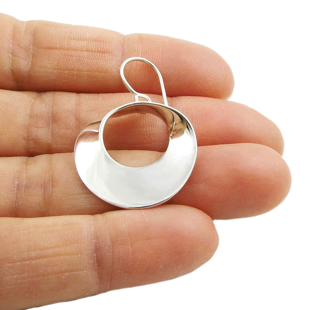 Wide sterling 925 silver moebius strip design circle loop earring held between fingers on a white background
