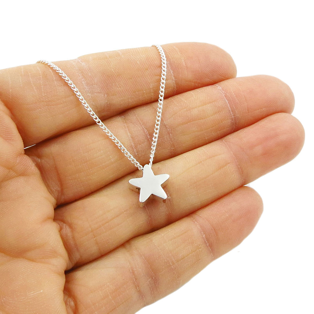 A hand holding a silver curb chain necklace with a three-dimensional star pendant.