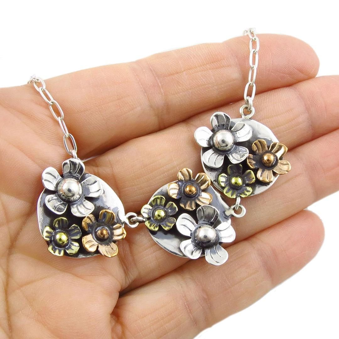 Floral necklace with silver, copper and gold flowers held in a hand against a white background