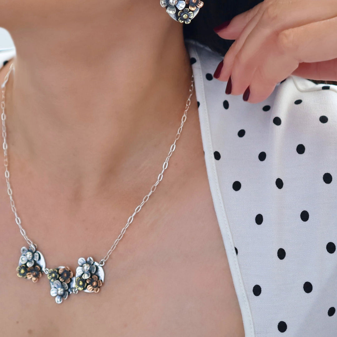 Silver and mixed metals floral necklace worn by a person with a polka dot top