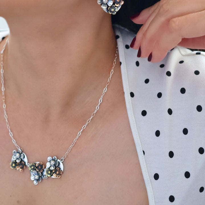 Silver and mixed metals floral necklace worn by a person with a polka dot top
