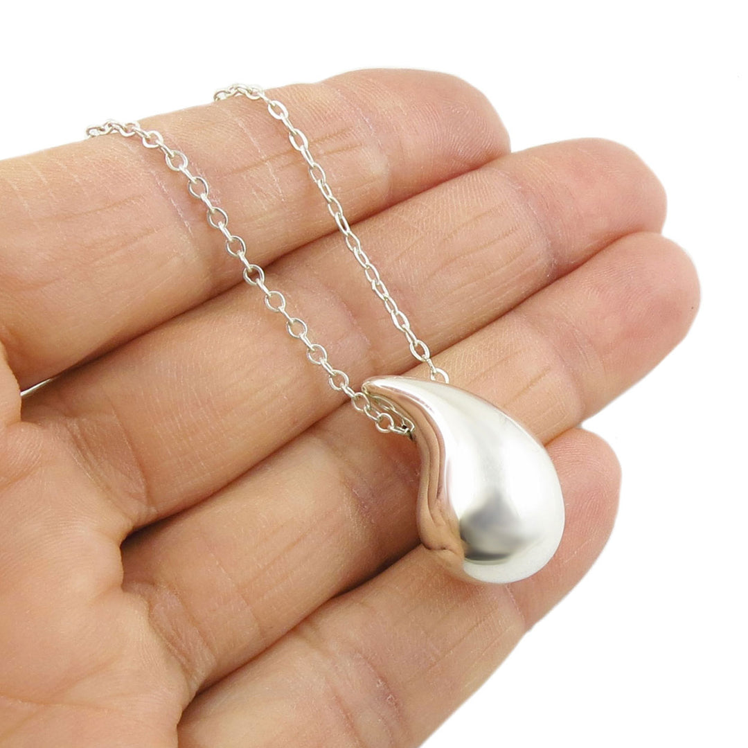 Silver teardrop pendant necklace held in a hand against a white background