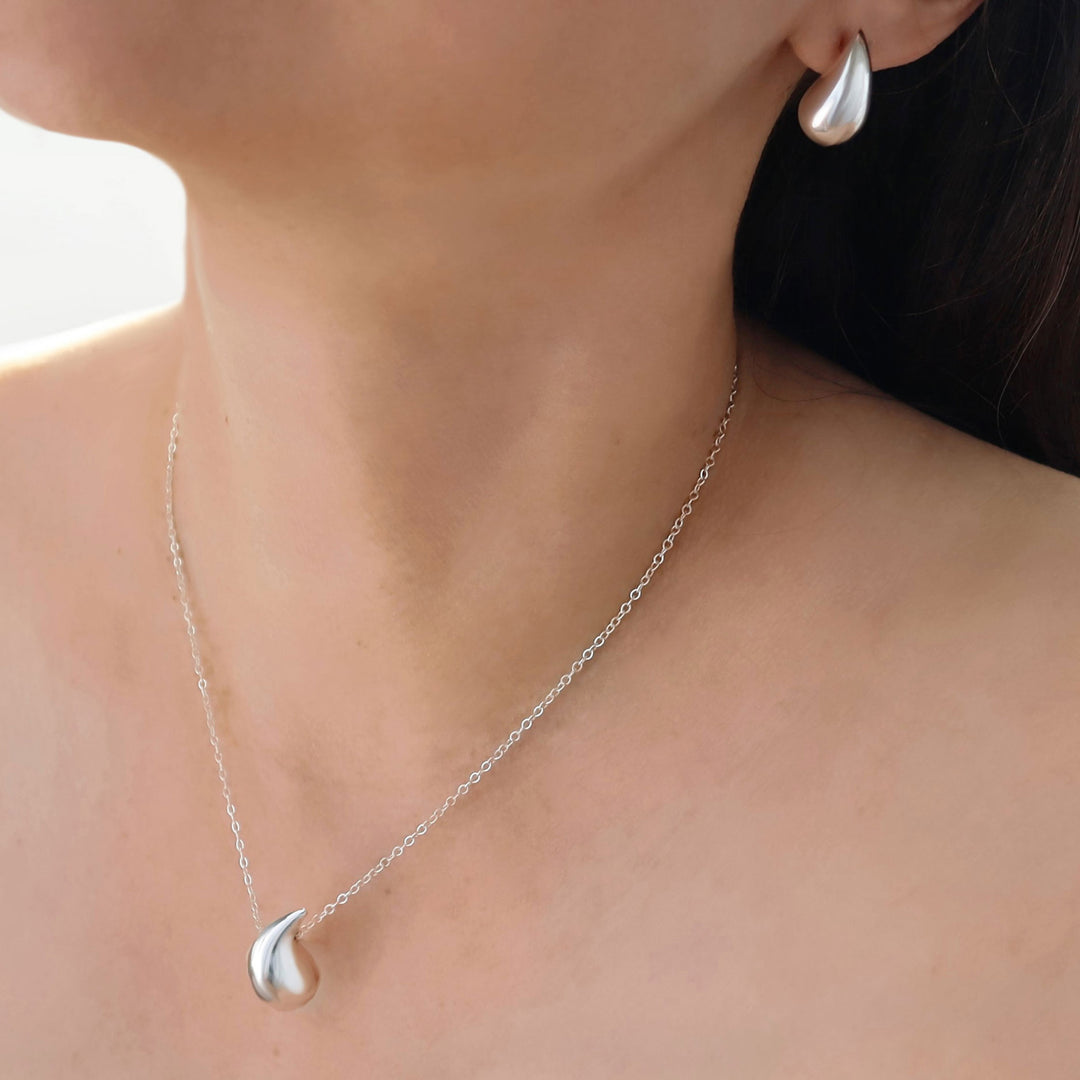Silver necklace and earring set on a person's neck and ear.