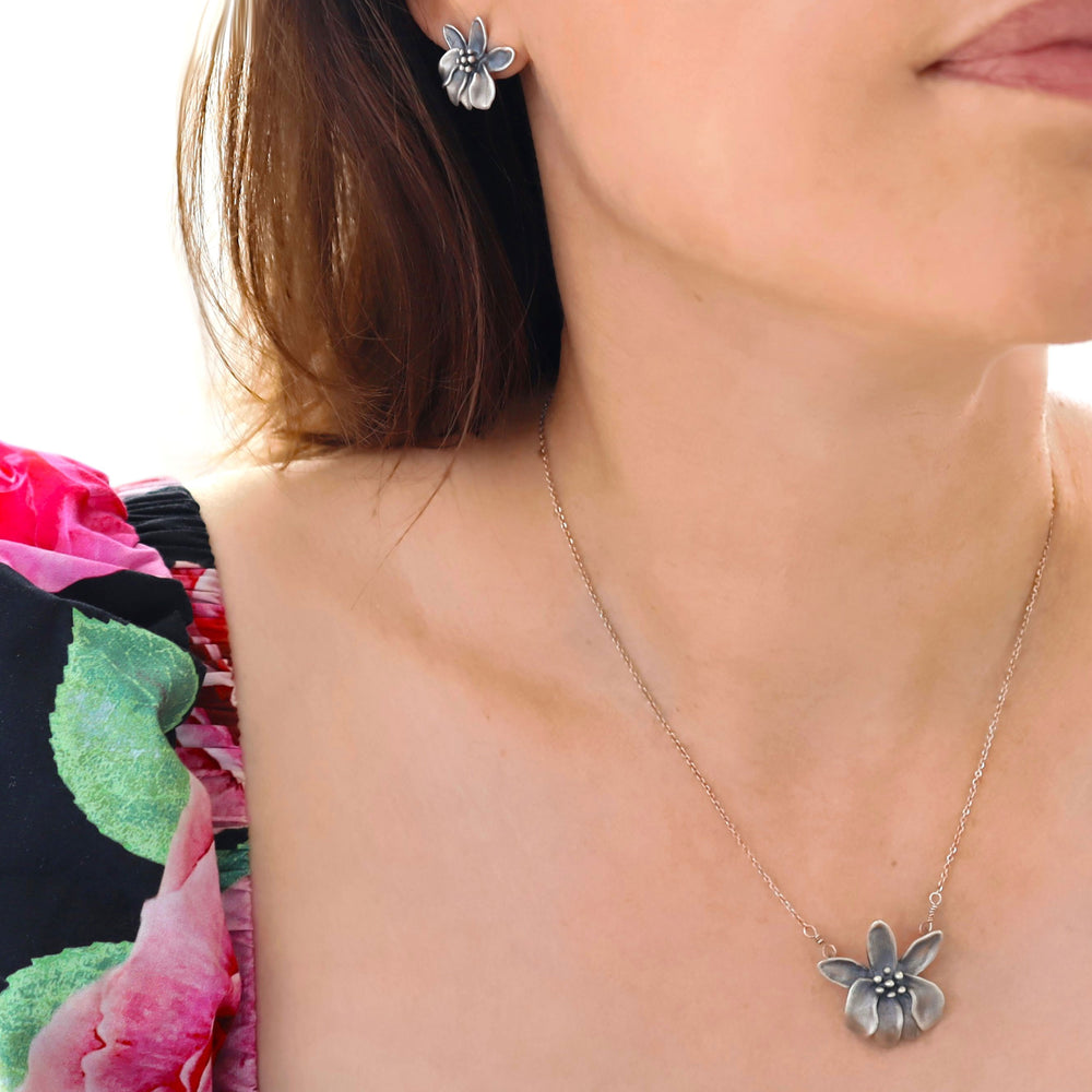 A woman wearing a silver moringa flower pendant and chain necklace and matching earrings. 
