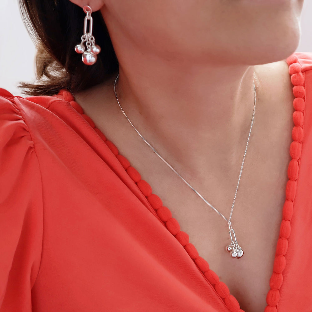 Long dangling 925 sterling silver ball bead necklace with matching earrings worn by a woman in an orange dress
