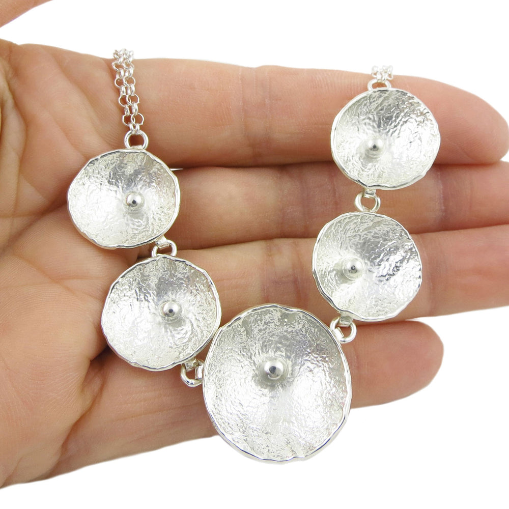 Silver necklace with poppy flowers on a hand against a white background