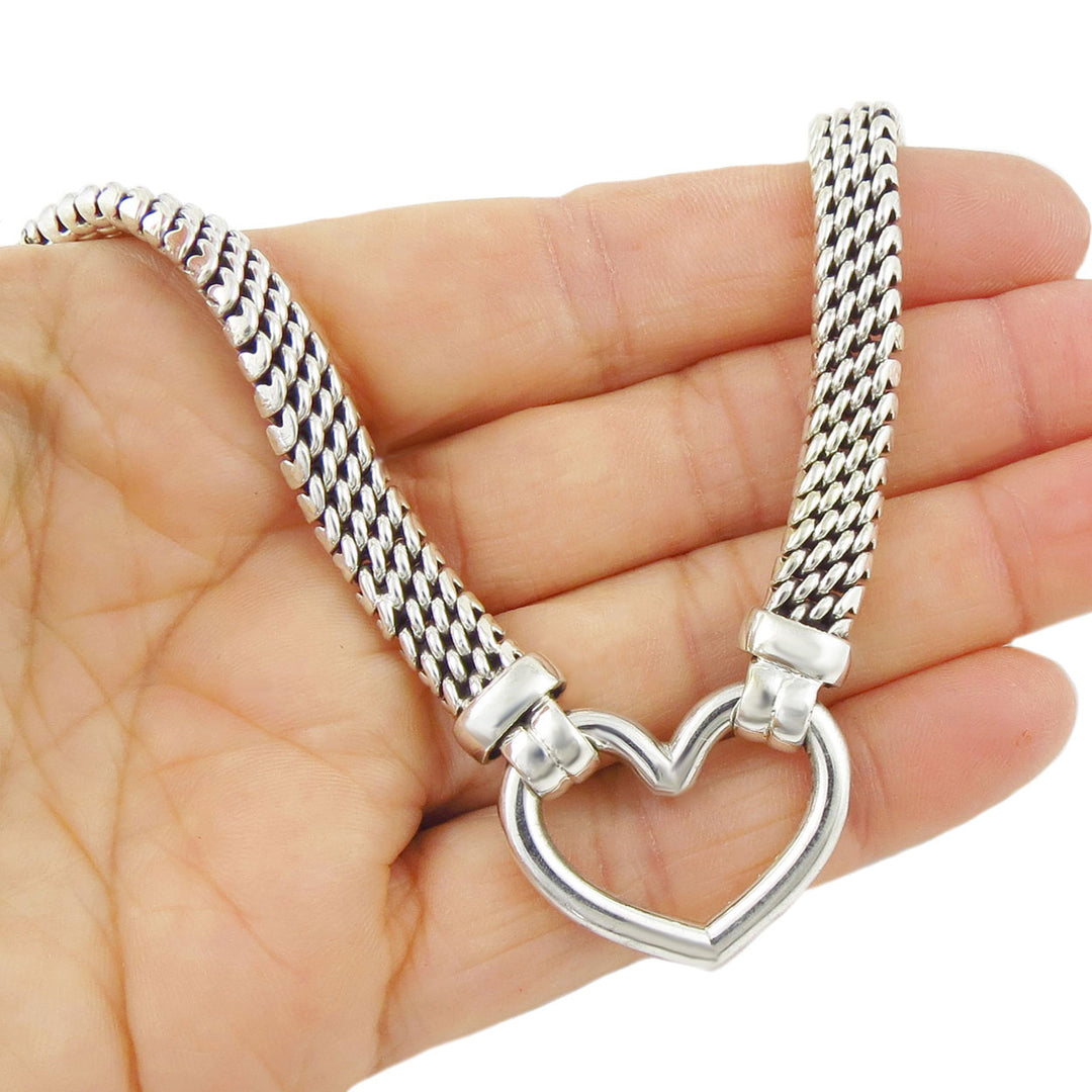 Silver chain necklace with a heart-shaped pendant held in a hand on a white background