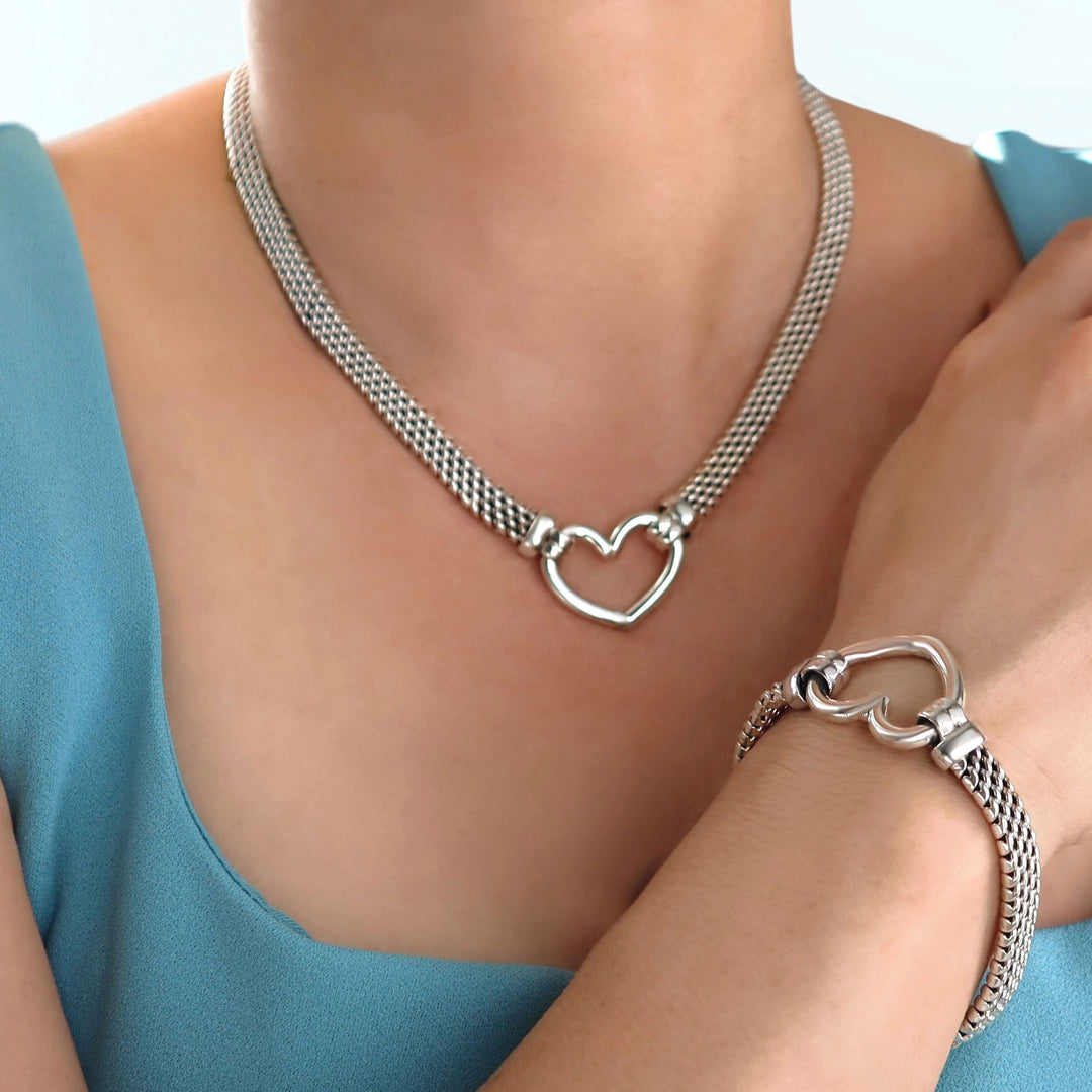 Silver necklace and bracelet with heart design on a person wearing a blue top.