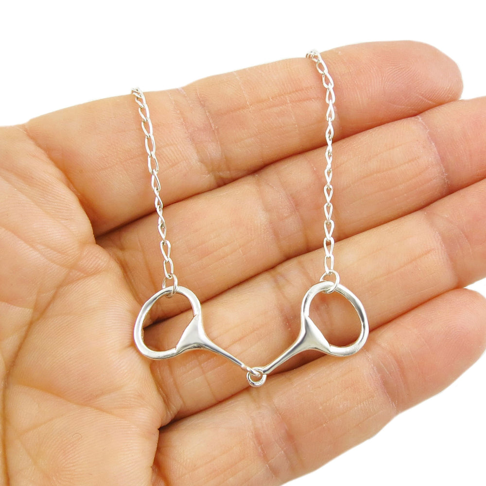 A hand holding a sterling silver horse snaffle bit pendant necklace on an adjustable chain.