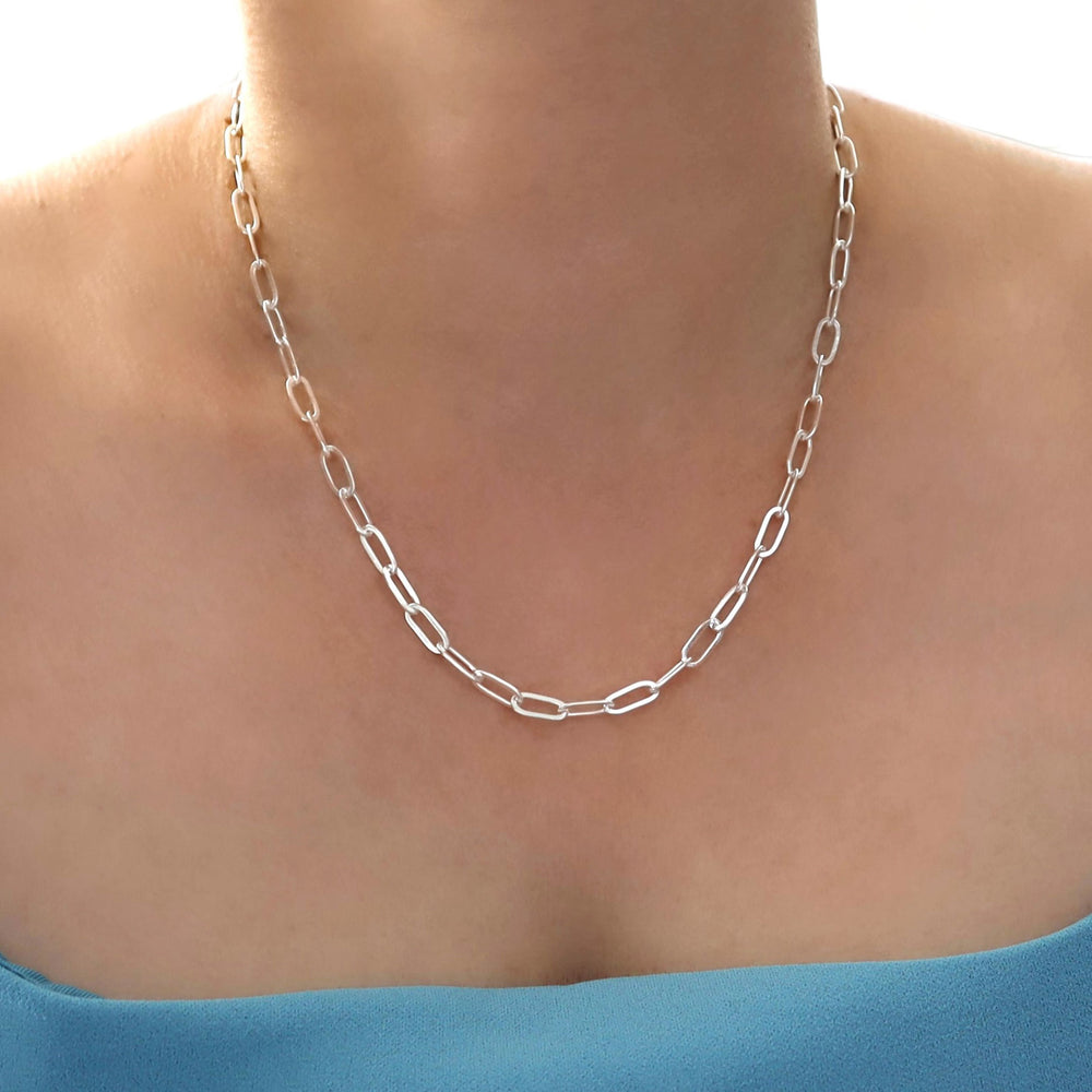 UK Sterling 925 silver paperclip chain necklace on a woman wearing a blue top against a neutral background
