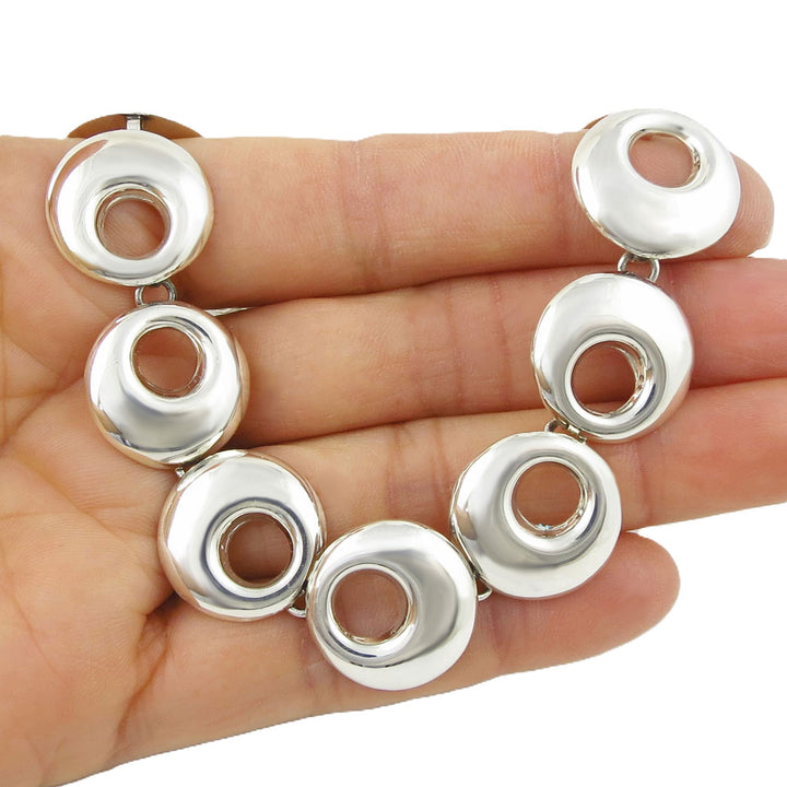 Silver necklace with circular design held on a hand against a white background