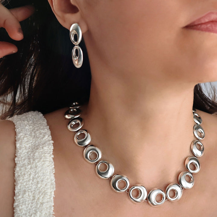 Silver necklace and earrings on a person wearing a white top