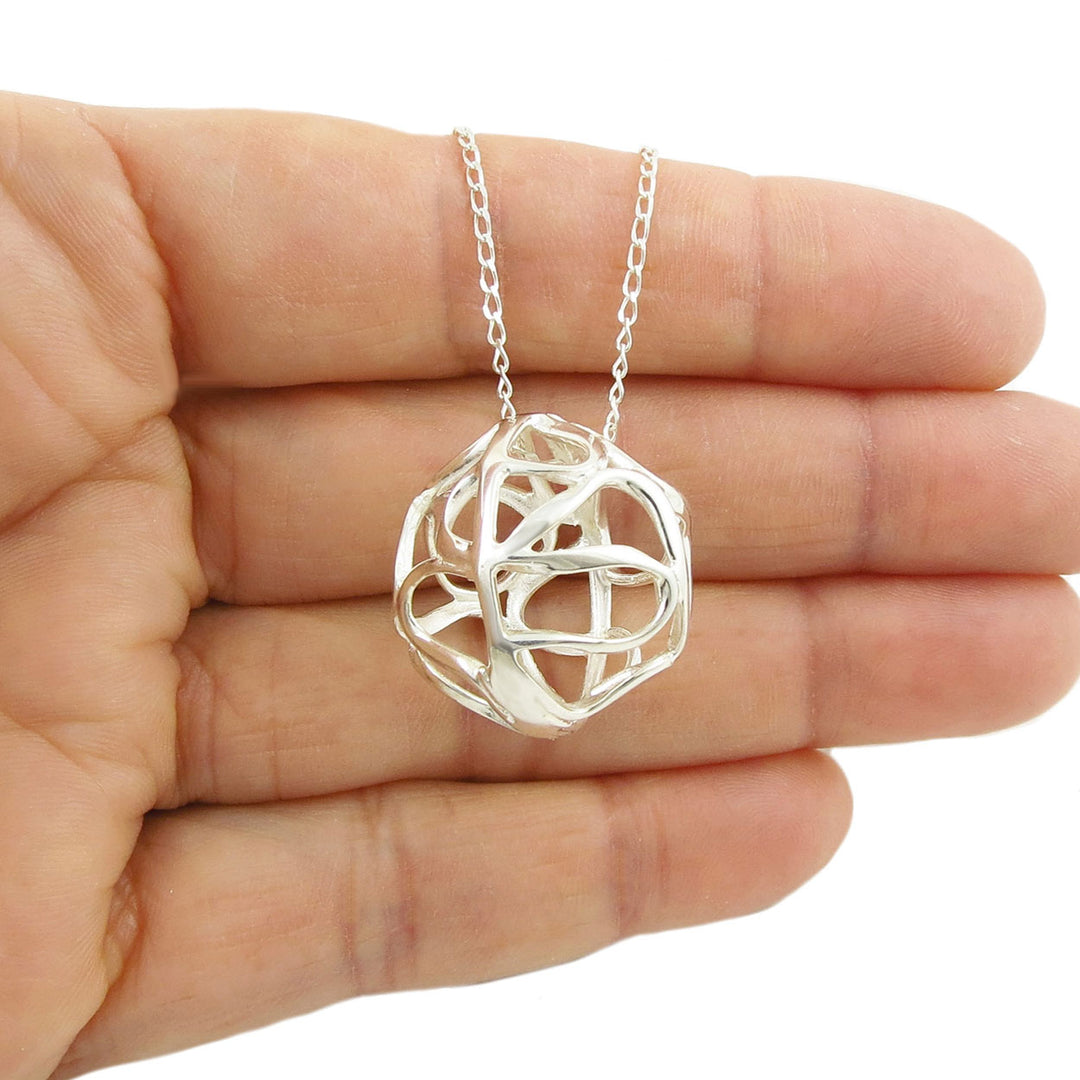 Silver necklace with a unique ball pendant held in a hand against a white background