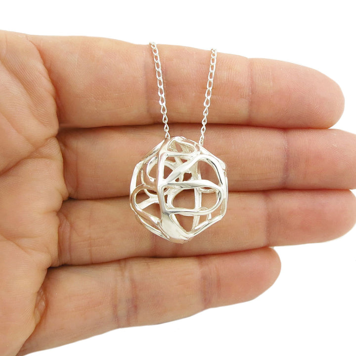 Silver necklace with a unique ball pendant held in a hand against a white background