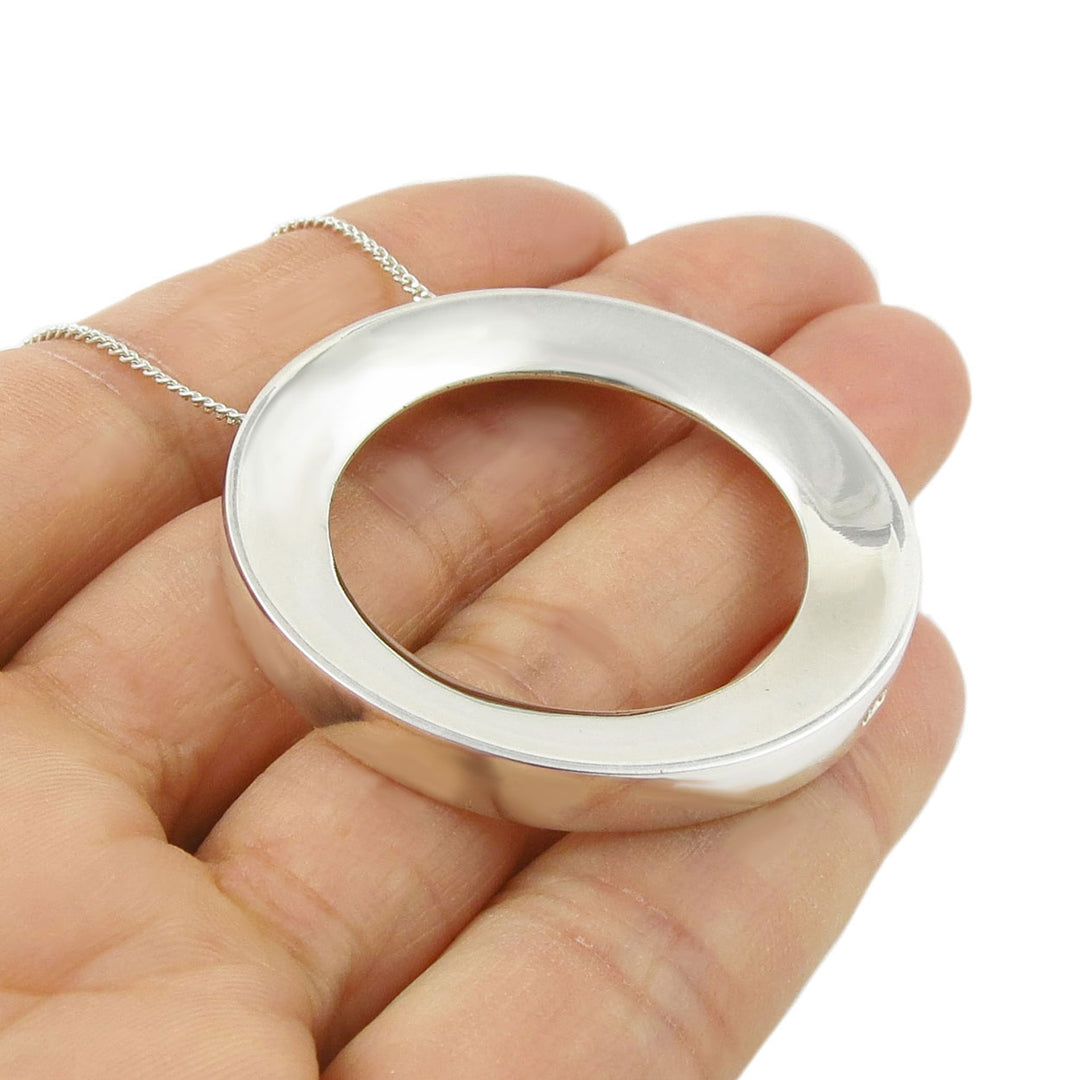 Silver circular pendant held in a hand against a white background