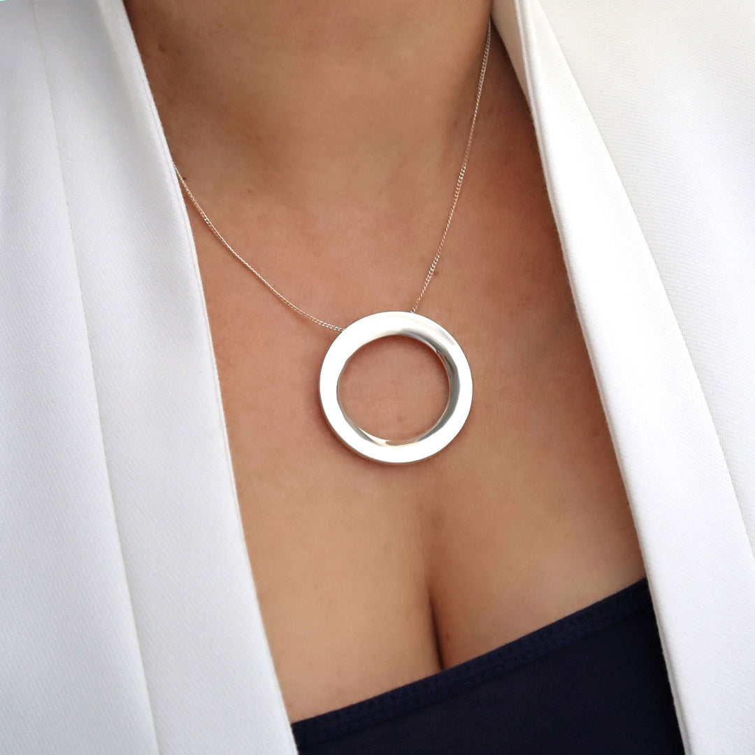 Silver necklace with a circular pendant worn by a person in a white blazer.