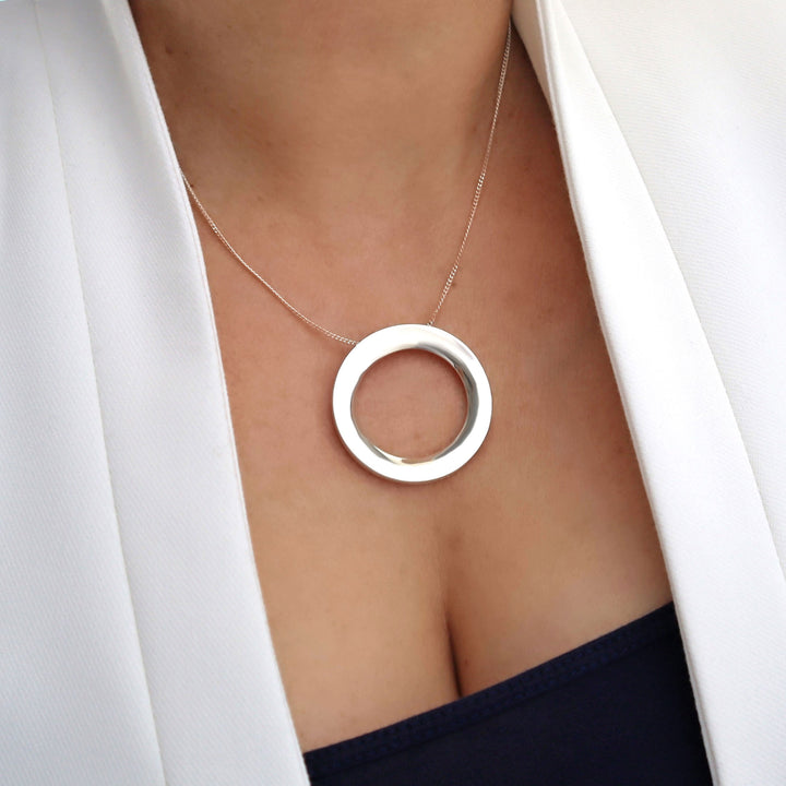 Silver necklace with a circular pendant worn by a person in a white blazer.