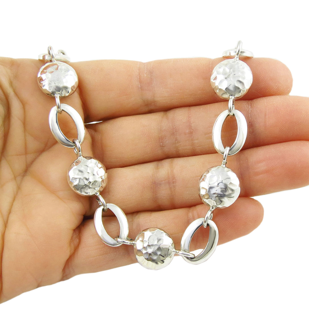 Silver bracelet with round and oval links held on a hand against a white background