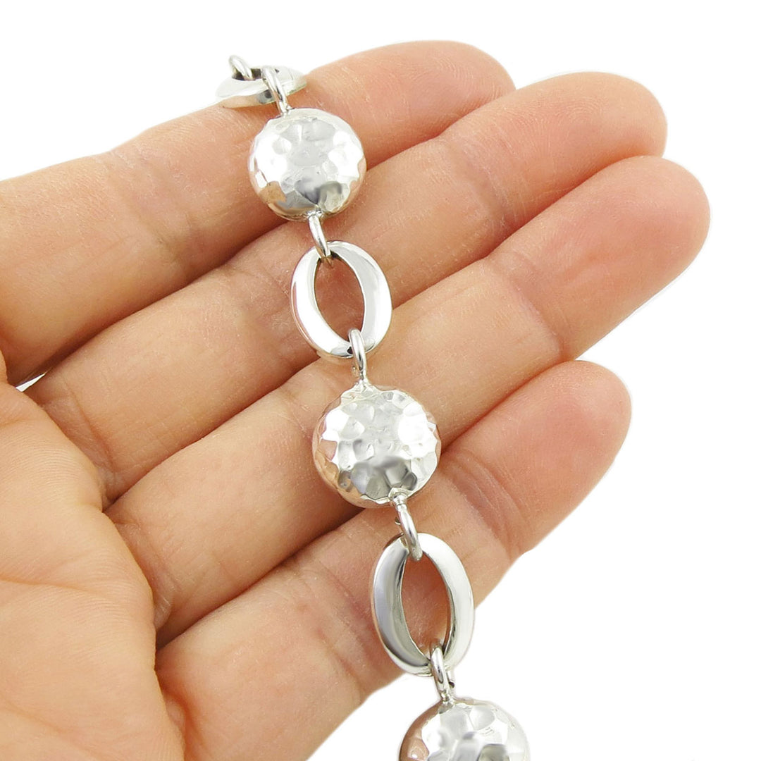 Silver necklace with round beads and oval links held in a hand against a white background