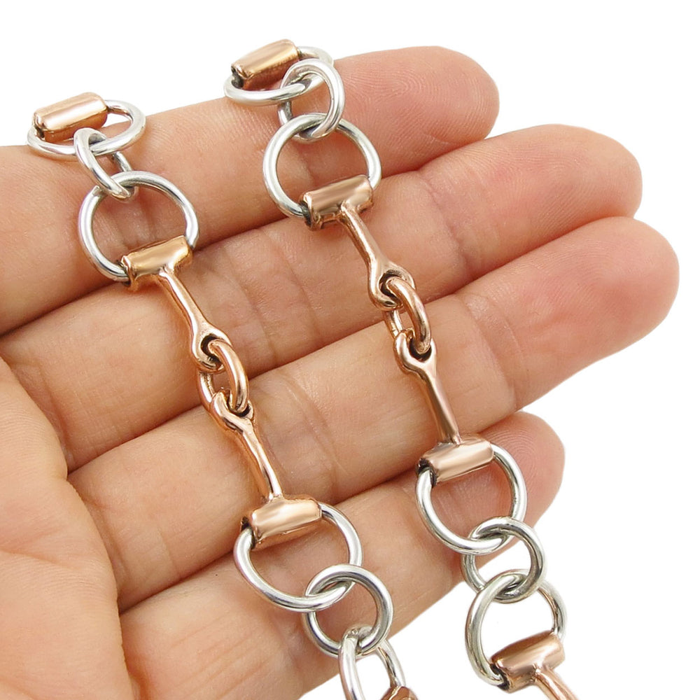 Copper and silver snaffle necklace held in a hand against a white background