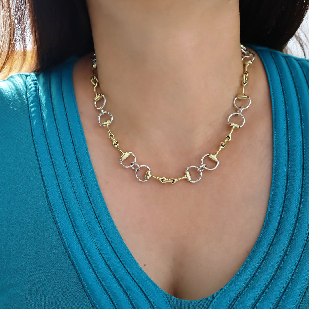 Gold and silver chain necklace worn by a person in a blue top