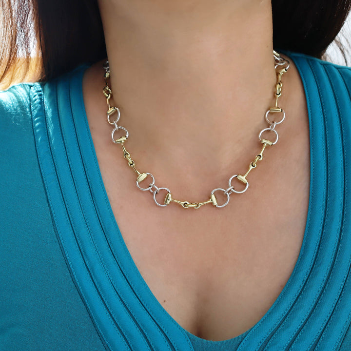 Gold and silver chain necklace worn by a person in a blue top