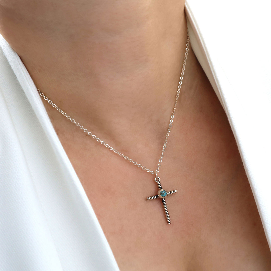 Silver necklace with a cross pendant on a person wearing a white top.