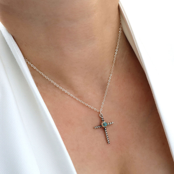 Silver necklace with a cross pendant on a person wearing a white top.