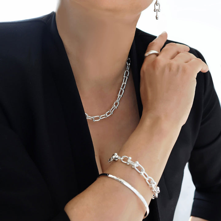 A woman wearing a silver gauge link chain necklace, bracelet and matching earrings on a plain background