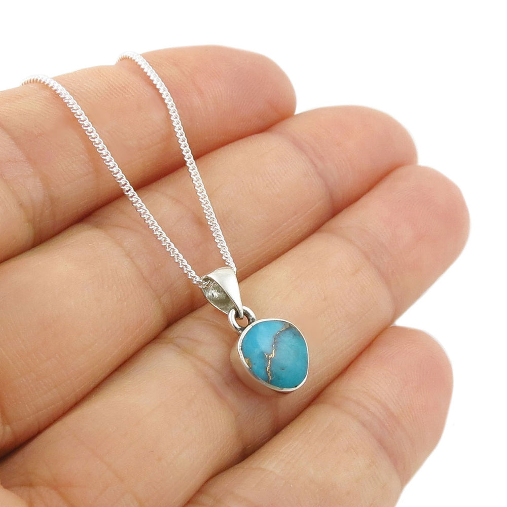 Silver necklace with a turquoise pendant held in a persons hand. 