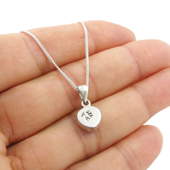 The reverse of a silver pendant necklace showing the 925 stamp, held in a person's hand. 