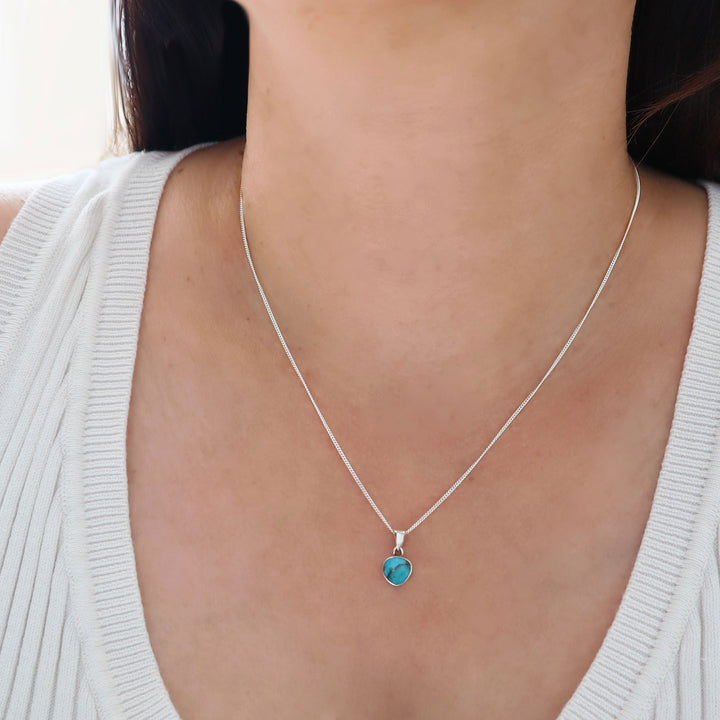 A woman wearing a silver pendant and chain necklace decorated with a turquoise gemstone. 