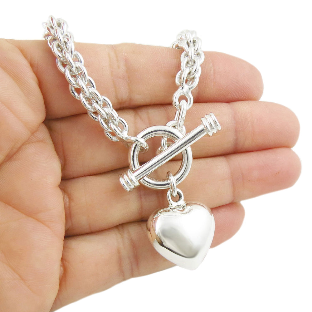 A heavy chunky sterling 925 silver triple link chain necklace with a t bar toggle and a puffy polished heart pendant held in a persons hand. 