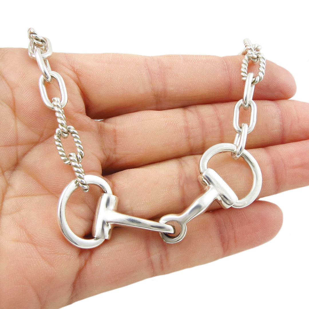 Silver chain with a horse bit design held in a hand against a white background