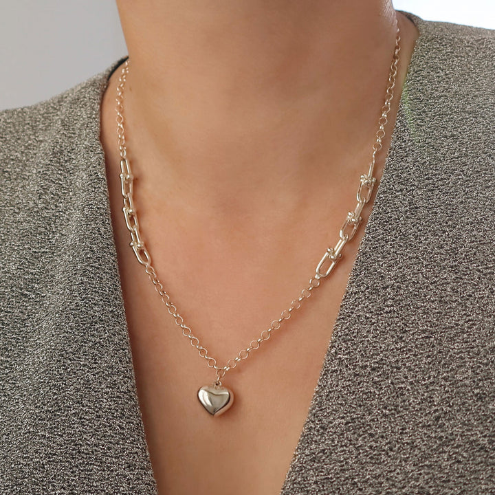 A long sterling 925 silver heart pendant and gauge link chain necklace worn by a women with a grey jacket. 