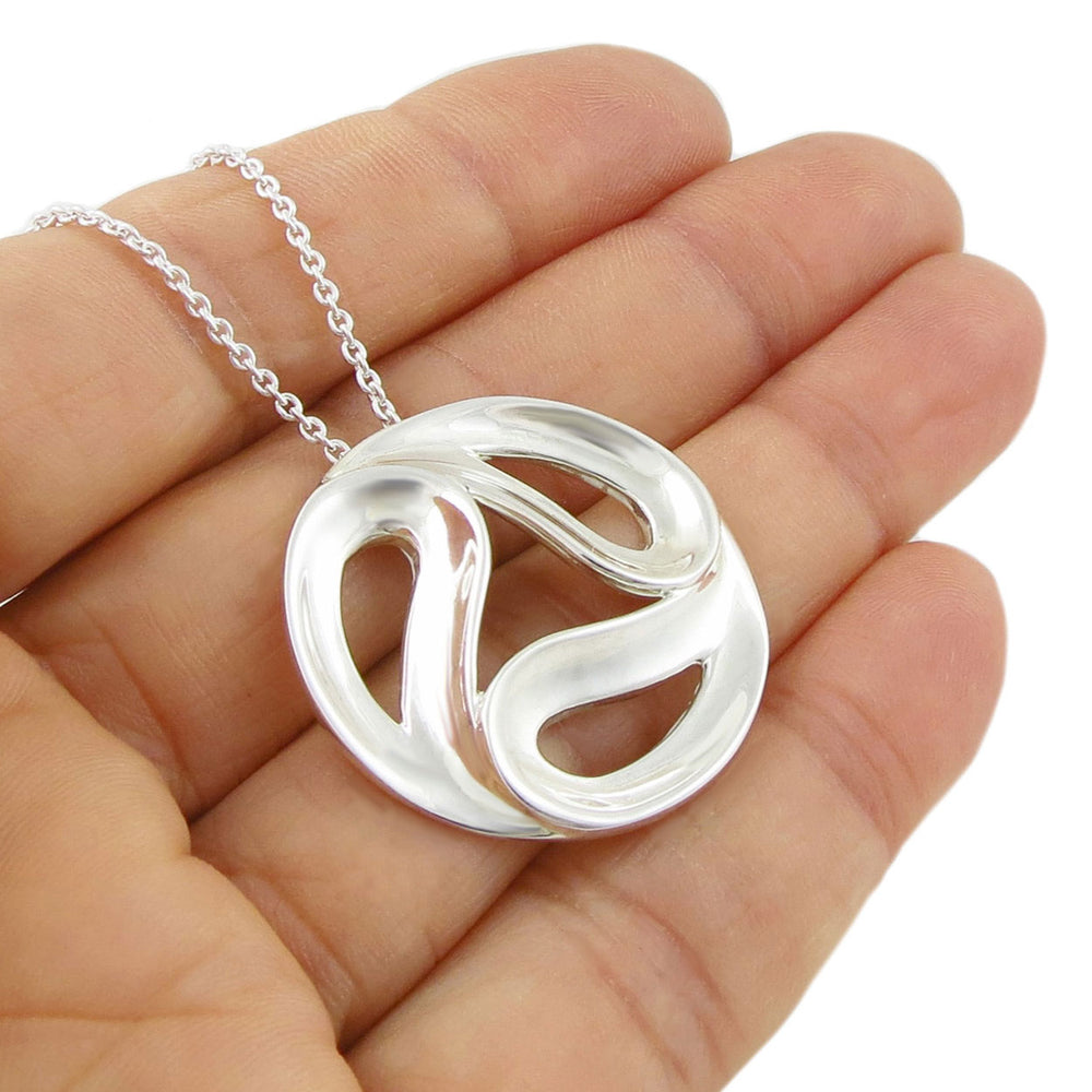 UK hallmarked 925 sterling silver necklace with a circular yin and yang pendant on a chain held in a hand against a white background