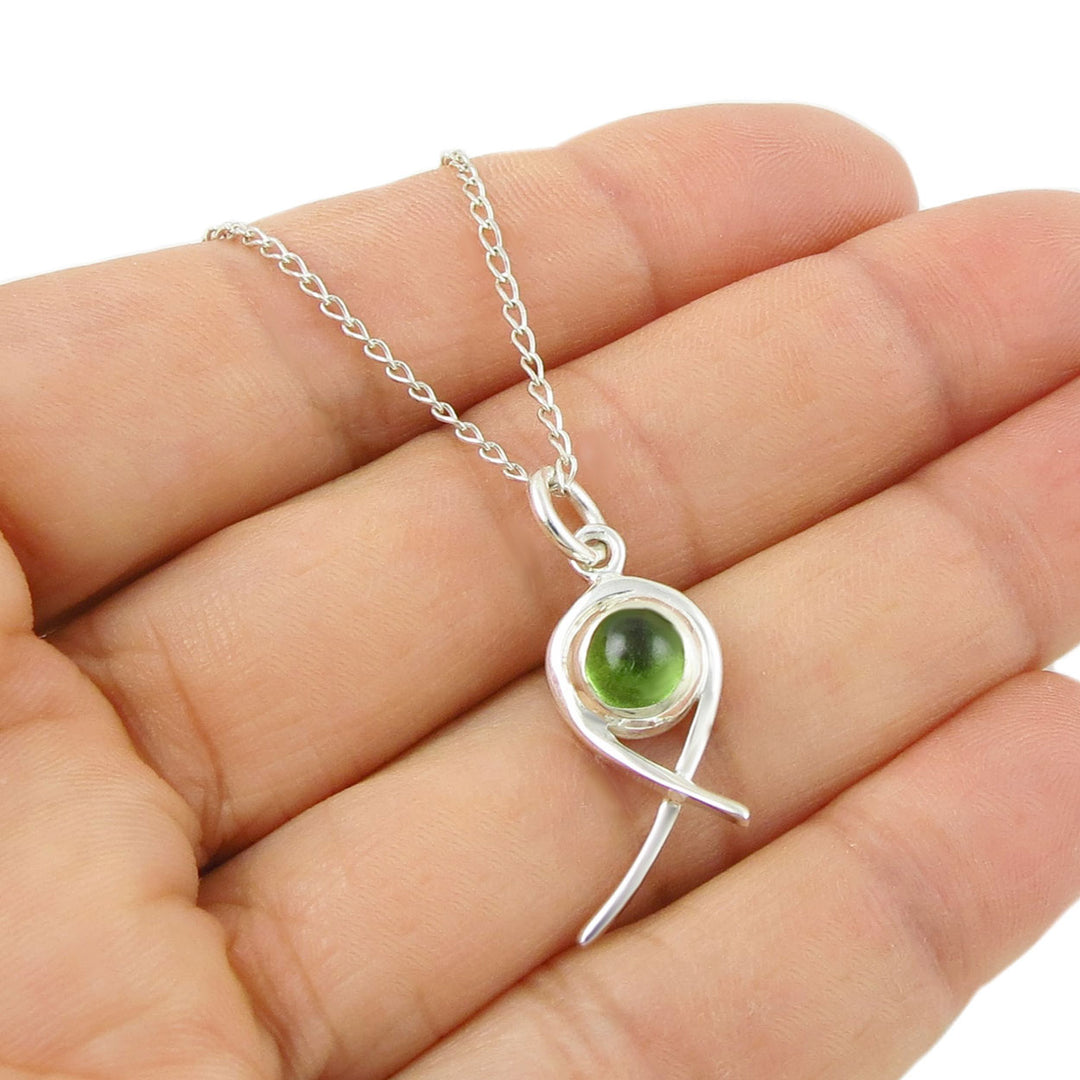 Sterling 925 Silver necklace with a green peridot gemstone birthstone pendant held in a hand on a white background