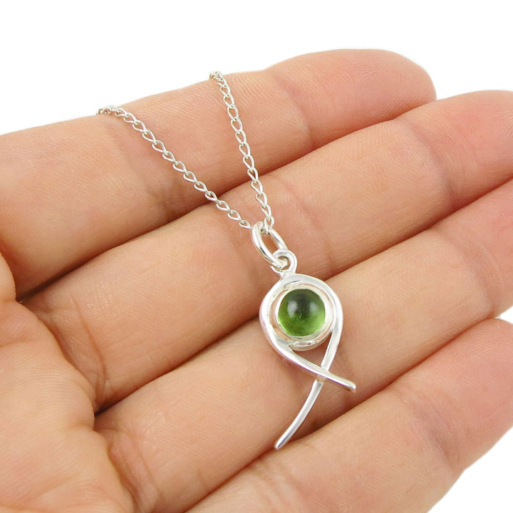 Sterling 925 Silver necklace with a green peridot gemstone birthstone pendant held in a hand on a white background