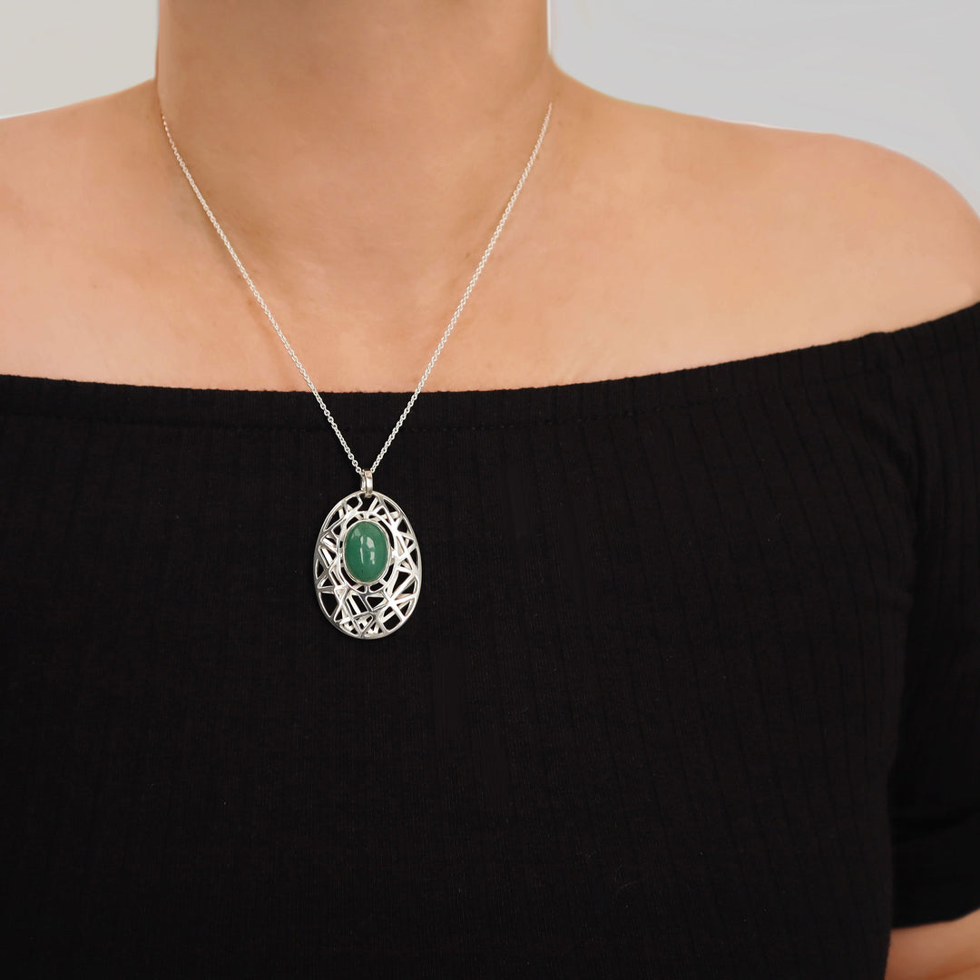 A large sterling 925 silver pendant and chain ecklace with a green gemstone pendant worn by a woman against a neutral background