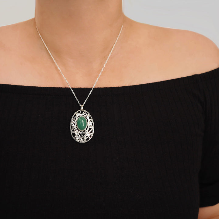 A large sterling 925 silver pendant and chain ecklace with a green gemstone pendant worn by a woman against a neutral background