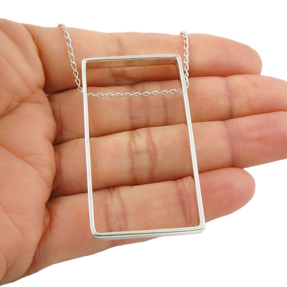 Sterling 925 Silver rectangular pendant necklace held in a woman's hand against a white background