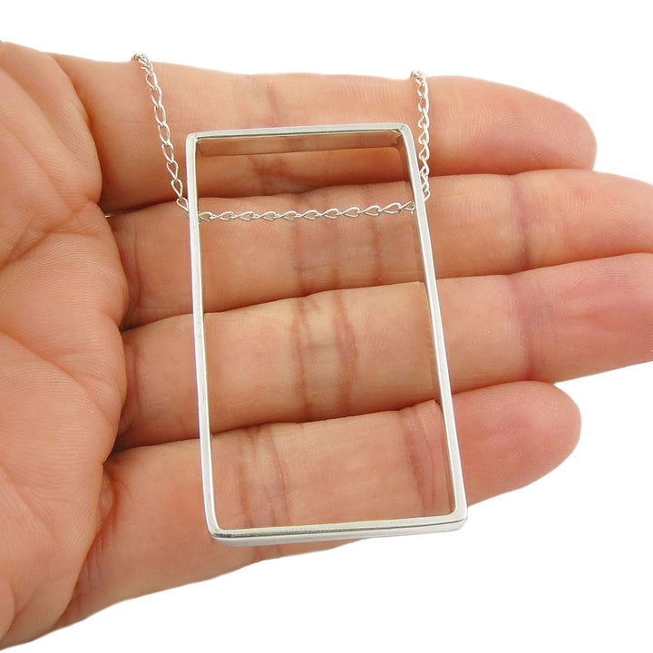 Sterling 925 Silver rectangular pendant necklace held in a woman's hand against a white background