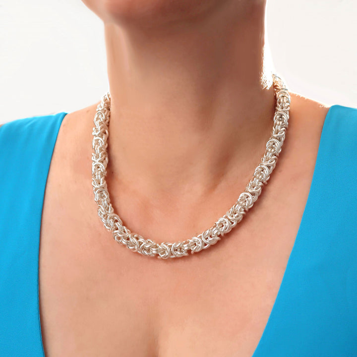 A woman in a blue top wearing a chunky thick 925 sterling silver byzantine chain necklace on a white background