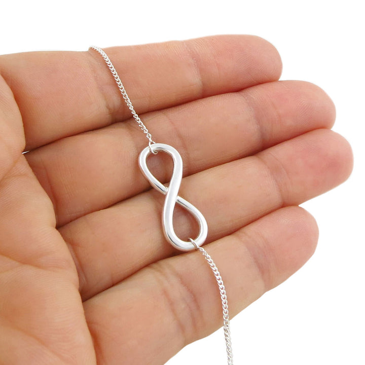 Infinity symbol necklace in sterling 925 silver held in a hand against a white background